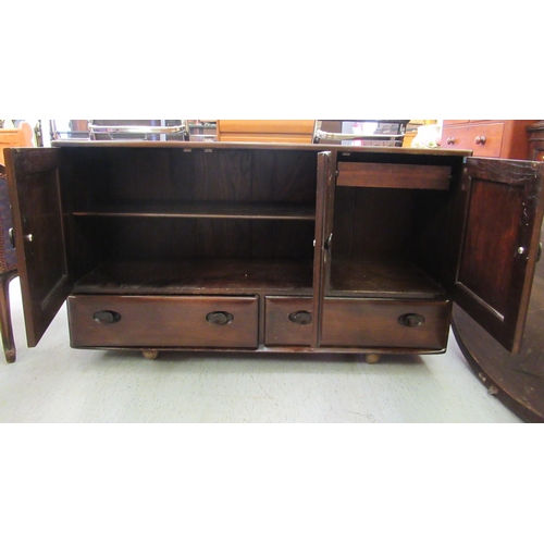 219 - An Ercol dark stained elm sideboard with three doors, over two inline drawers, on a plinth and caste... 