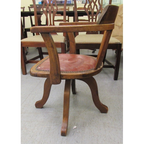 299 - An early 20thC stained beech framed, open arm desk chair, the stud upholstered hide seat raised on a... 