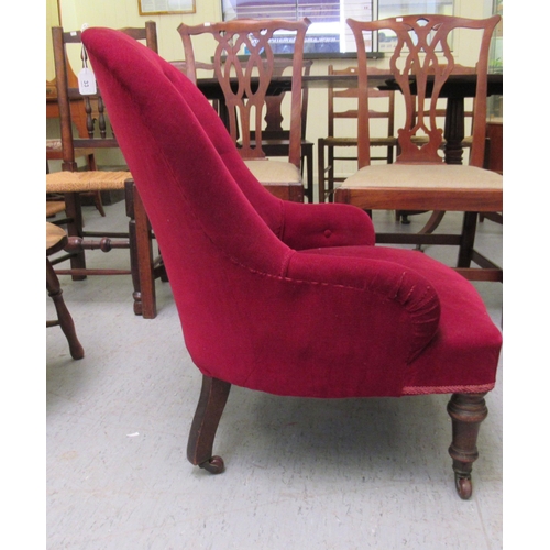 33 - An early 20thC nursing chair, upholstered in red fabric, raised on turned forelegs and castors