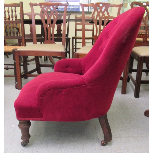 33 - An early 20thC nursing chair, upholstered in red fabric, raised on turned forelegs and castors