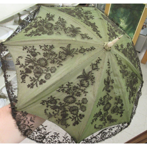 23 - An Edwardian cream coloured and green satin parasol with a black lace finish, on a simulated ivory a... 