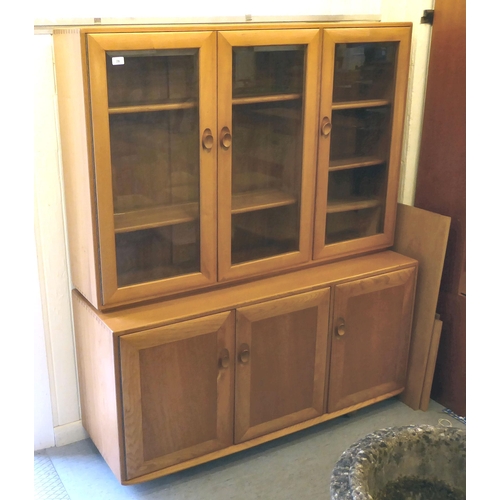 78 - An Ercol two part blonde elm cabinet, the upper part having three inline clear bevelled glass panell... 