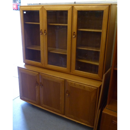 78 - An Ercol two part blonde elm cabinet, the upper part having three inline clear bevelled glass panell... 