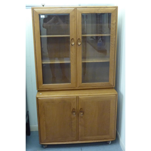 80 - An Ercol two part blonde elm cabinet, the upper part having a pair of clear bevelled glass panelled ... 