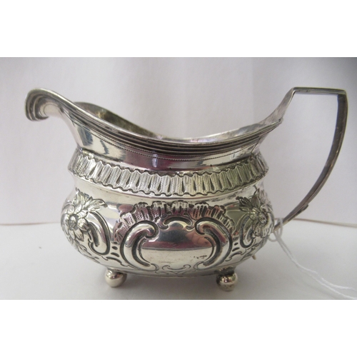 94 - A George III silver oval cream jug, embossed and chased with flora and scrolls, on ball feet  London... 