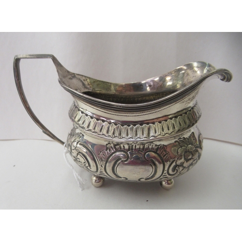 94 - A George III silver oval cream jug, embossed and chased with flora and scrolls, on ball feet  London... 