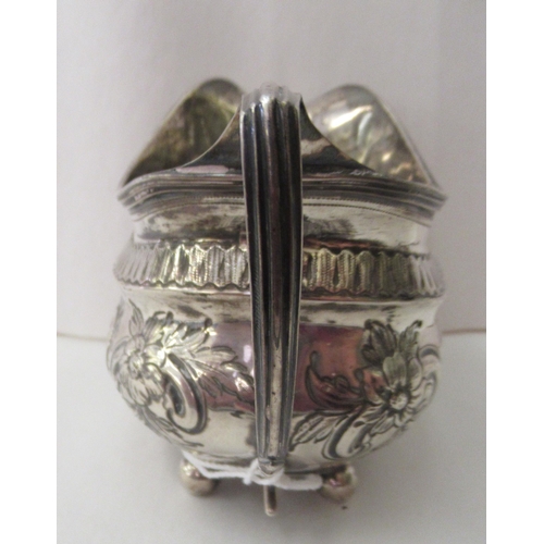 94 - A George III silver oval cream jug, embossed and chased with flora and scrolls, on ball feet  London... 