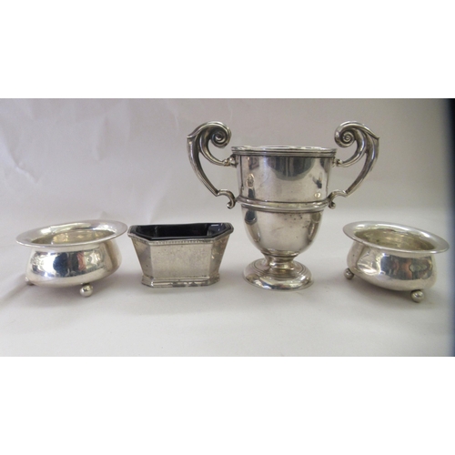 221 - An early 20thC silver twin handled small pedestal trophy cup; and a pair of silver salt cellars, on ... 