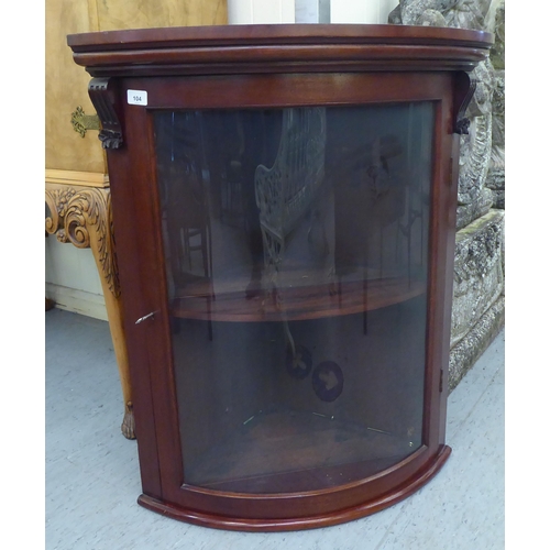 104 - A late 19thC mahogany hanging quadrant cupboard, the lockable glazed, full height door enclosing a s... 