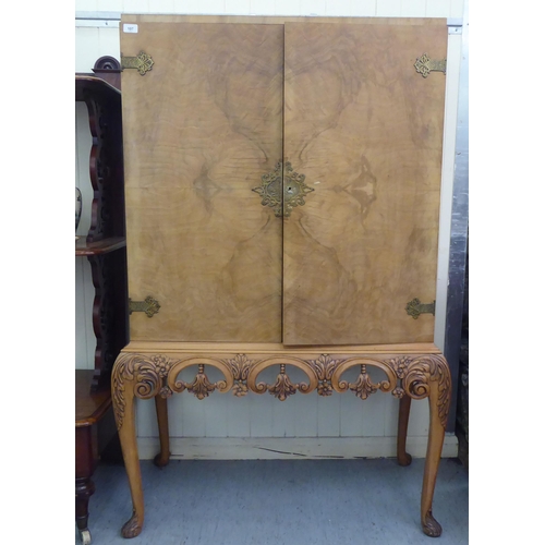 107 - A mid 20thC bleached walnut cocktail cabinet with decoratively pierced and engraved brass mounts, th... 