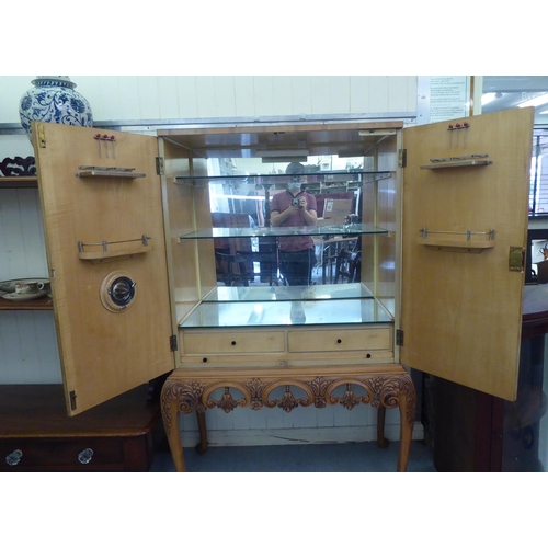 107 - A mid 20thC bleached walnut cocktail cabinet with decoratively pierced and engraved brass mounts, th... 