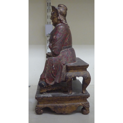 185 - A late 19thC/early 20thC Chinese lacquered and overpainted wooden figure, a man seated on a stool  1... 