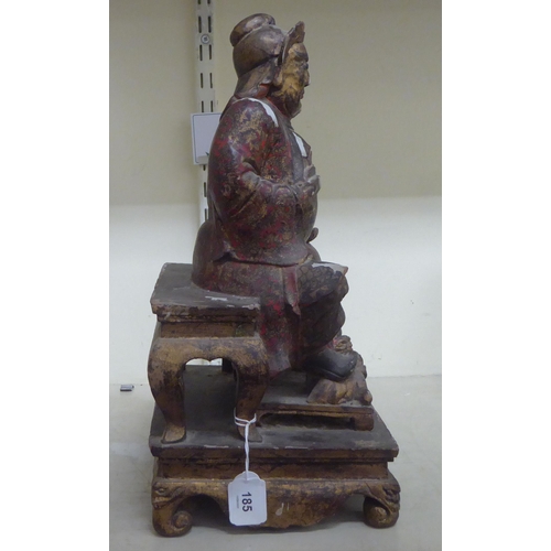 185 - A late 19thC/early 20thC Chinese lacquered and overpainted wooden figure, a man seated on a stool  1... 