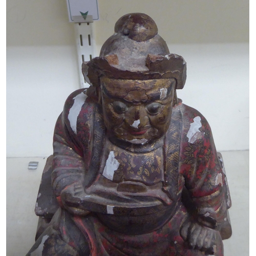 185 - A late 19thC/early 20thC Chinese lacquered and overpainted wooden figure, a man seated on a stool  1... 