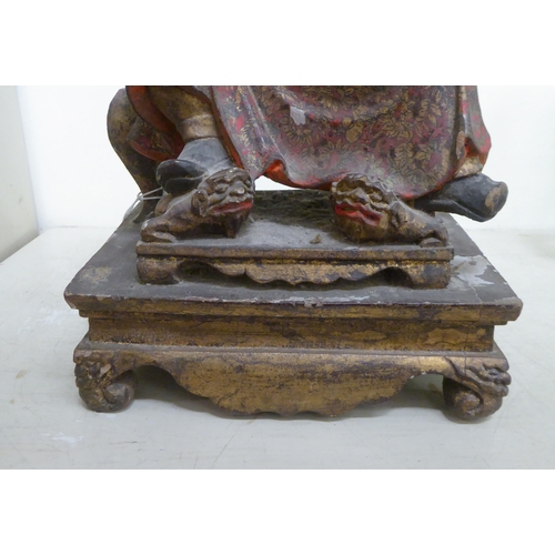 185 - A late 19thC/early 20thC Chinese lacquered and overpainted wooden figure, a man seated on a stool  1... 