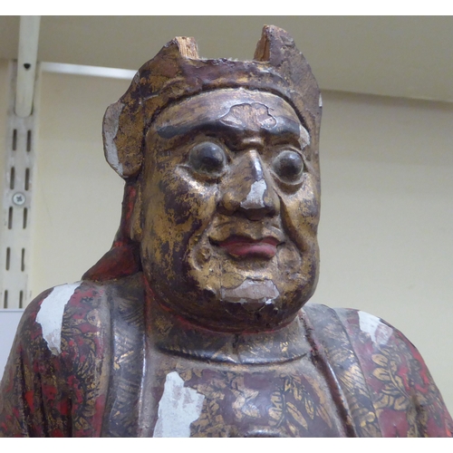 185 - A late 19thC/early 20thC Chinese lacquered and overpainted wooden figure, a man seated on a stool  1... 