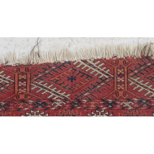 39 - A Bokhara rug, decorated with three columns of seven guls, bordered by stylised designs, on a red gr... 