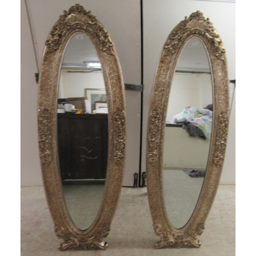 66 - A pair of Victorian style oval dressing mirrors, set in ornately moulded gilt frames, on folding eas... 