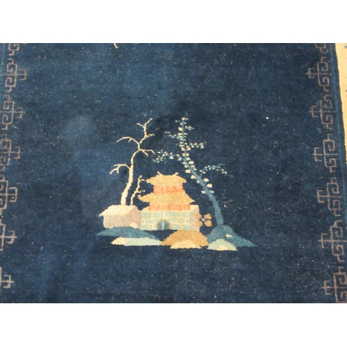 88 - A Chinese woollen rug, decorated with buildings within a border of flora and birds, on a blue ground... 