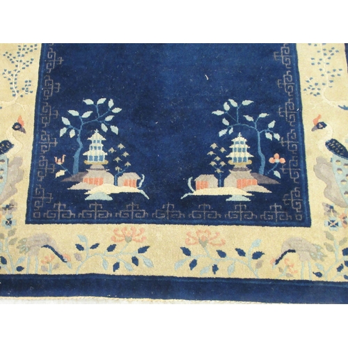 88 - A Chinese woollen rug, decorated with buildings within a border of flora and birds, on a blue ground... 