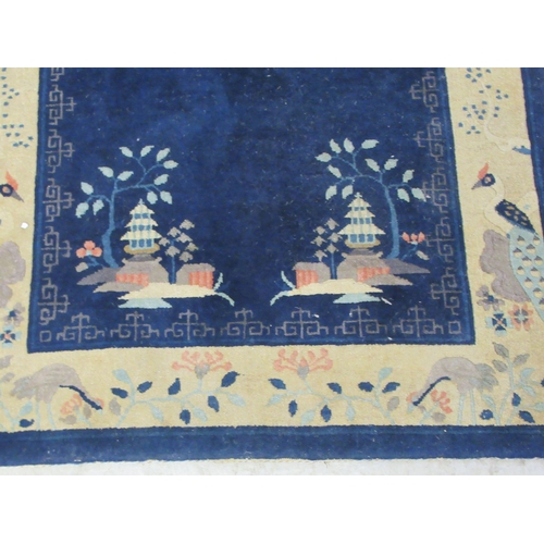 88 - A Chinese woollen rug, decorated with buildings within a border of flora and birds, on a blue ground... 