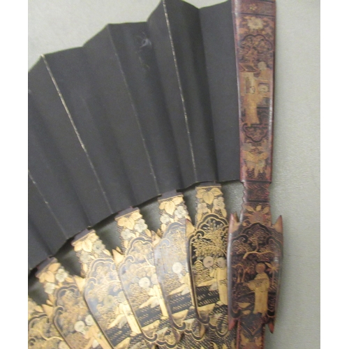 100 - An early 20thC Chinese lacquered and gilded fan, the sticks incorporating standing figures  the guar... 