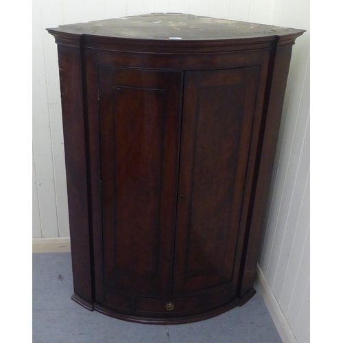 260 - A George III mahogany hanging quadrant corner cabinet with a moulded cornice, over a pair of panelle... 