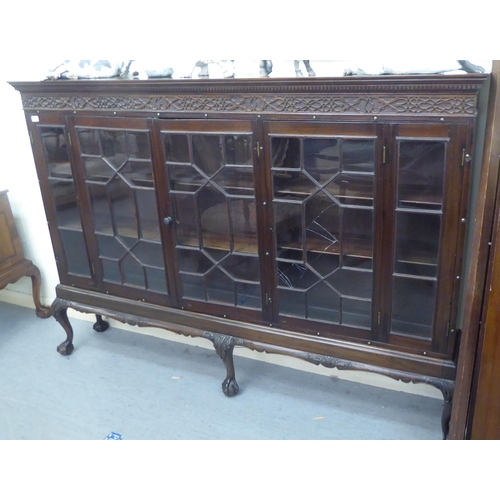 86 - A 1920s mahogany bookcase with a level top and blint fret carved frieze, over astragal glazed doors,... 