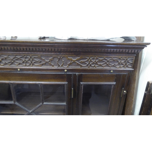 86 - A 1920s mahogany bookcase with a level top and blint fret carved frieze, over astragal glazed doors,... 