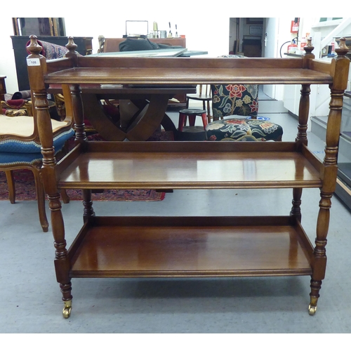 108 - An early 20thC mahogany three tier buffet, united by turned and block pillar supports, on brass cap ... 