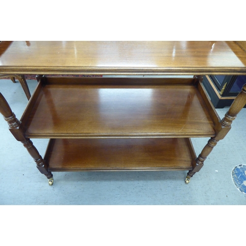 108 - An early 20thC mahogany three tier buffet, united by turned and block pillar supports, on brass cap ... 