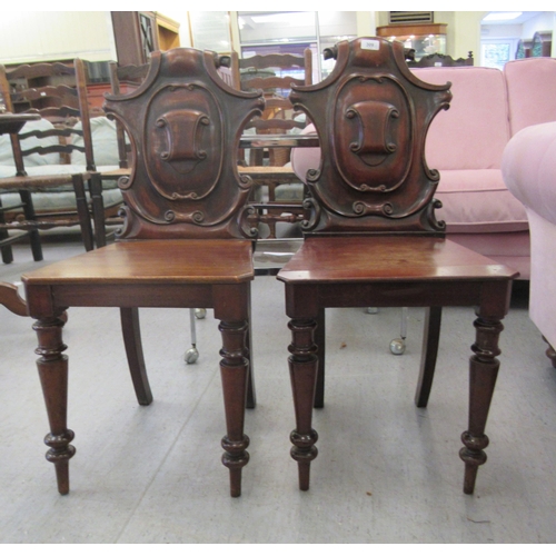 137 - A pair of late Victorian mahogany framed hall chairs with C-scroll carved solid backs and seats, rai... 