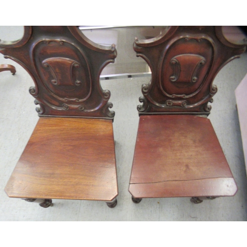 137 - A pair of late Victorian mahogany framed hall chairs with C-scroll carved solid backs and seats, rai... 