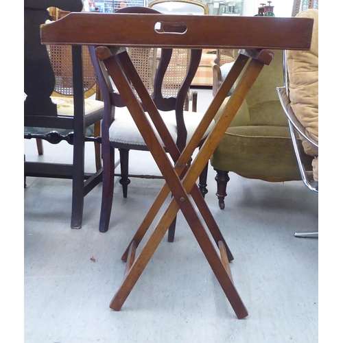 144 - A late 19thC mahogany butler's tray with opposing cut-out handles, raised on a folding crossover sta... 