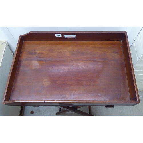 144 - A late 19thC mahogany butler's tray with opposing cut-out handles, raised on a folding crossover sta... 