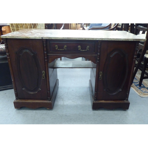 164 - A late Victorian design mahogany desk with a marble top, over a drawer and two cupboard doors, on a ... 