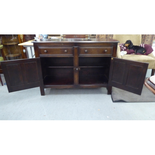 173 - A (probably) Ercol dark stained elm sideboard with a pair of frieze drawers, over two panelled doors... 