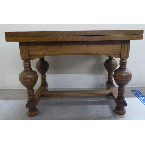 185 - A mid 20thC oak draw leaf occasional table, raised on turned, block supports, united by a stretcher&... 