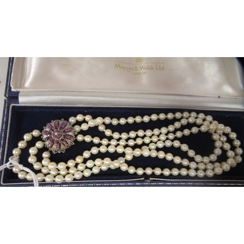 28 - A triple row pearl choker, on a white metal ruby and diamond set rosette clasp 