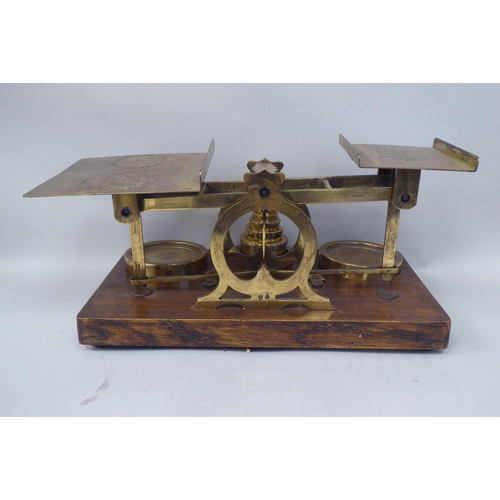 332 - Early 20thC lacquered brass beam balance type postal scales, on a rectangular oak platform, the two ... 