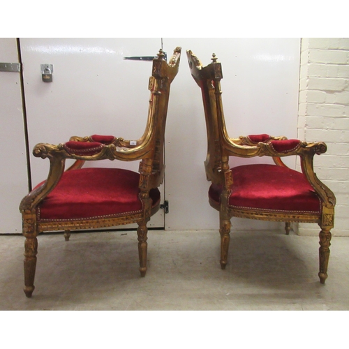 360 - A pair of late Victorian style gilded, moulded and carved salon chairs with open arms and part butto... 