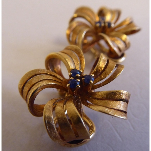 111 - A pair of textured 18ct gold ribbon tied floral clip-on earrings, claw set with sapphires