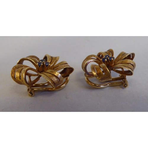 111 - A pair of textured 18ct gold ribbon tied floral clip-on earrings, claw set with sapphires