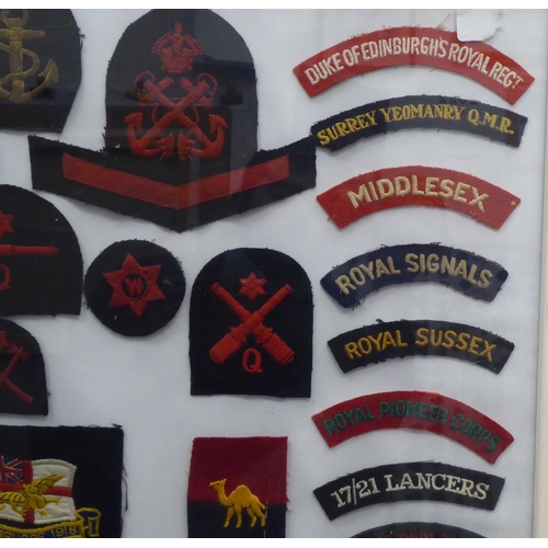 20 - A framed display of woven and other military uniform badges and similar insignia, some copies: to in... 