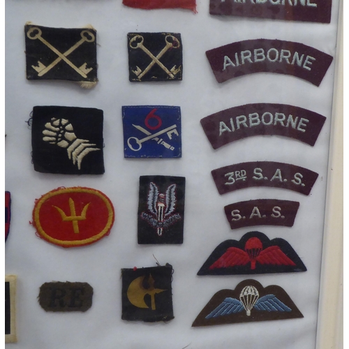 20 - A framed display of woven and other military uniform badges and similar insignia, some copies: to in... 