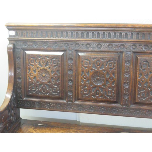 139 - A late Victorian profusely carved oak settle with a high, level, quadruple fielded panelled back and... 