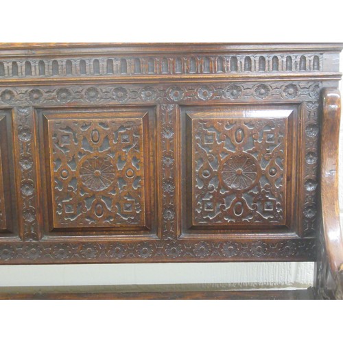 139 - A late Victorian profusely carved oak settle with a high, level, quadruple fielded panelled back and... 