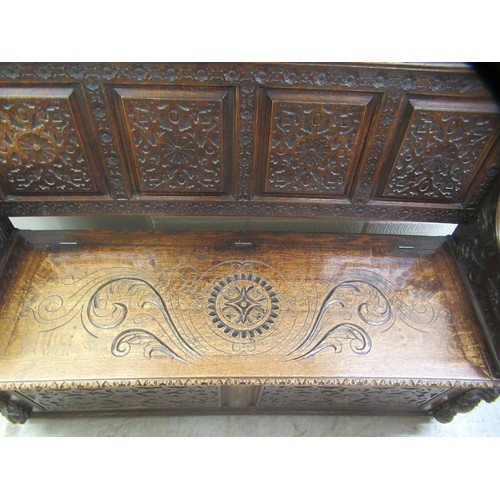 139 - A late Victorian profusely carved oak settle with a high, level, quadruple fielded panelled back and... 