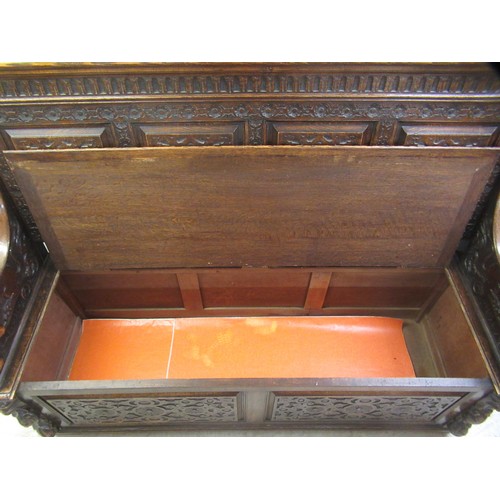 139 - A late Victorian profusely carved oak settle with a high, level, quadruple fielded panelled back and... 