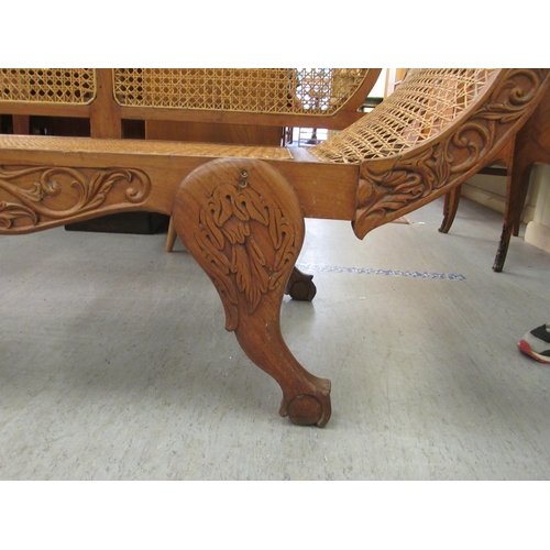 121 - A late 19thC Indian Colonial carved fruitwood framed scroll end settee with a woven split cane panel... 